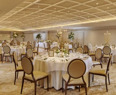 Elegant hotel ballroom with round tables, chic centrepieces, ambient lighting, ideal for weddings and events.