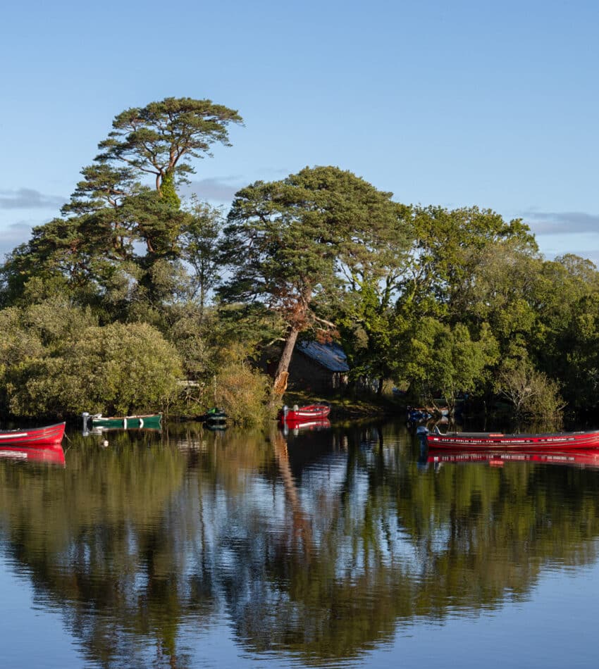 Serene lake view with vibrant red canoes, lush greenery, and tranquil waters, perfect for relaxation and nature activities.