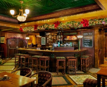 Cosy hotel bar with festive decor, inviting wooden seating, ornate ceilings, and a well-stocked drinks menu, perfect for relaxation.