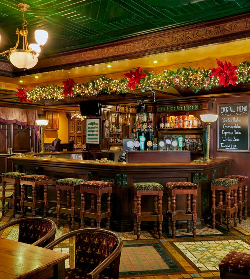 Cosy hotel bar with festive decor, inviting wooden seating, ornate ceilings, and a well-stocked drinks menu, perfect for relaxation.
