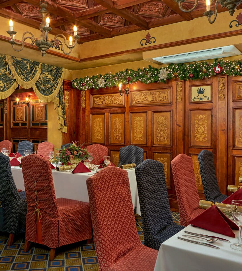 Elegant hotel dining room with ornate wooden decor, festive garlands, and finely set tables, perfect for a cosy meal.