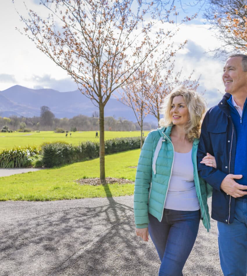 Couple enjoying scenic mountain view in lush hotel garden, surrounded by blossoming trees and vibrant greenery.