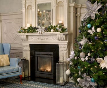 Cosy lounge with a decorated Christmas tree, elegant fireplace, and a plush blue armchair for a festive retreat.