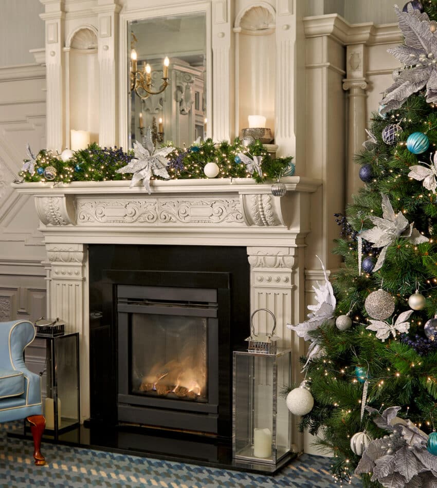 Cosy lounge with a decorated Christmas tree, elegant fireplace, and a plush blue armchair for a festive retreat.