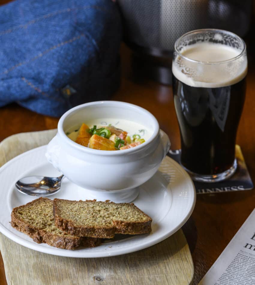 Warm seafood chowder with brown bread, Irish stout, and a cosy ambience at a traditional hotel pub table.