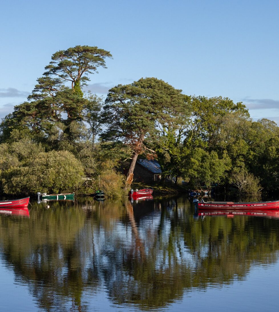 Serene lake view with red boats, lush trees, and clear skies, offering peaceful ambience for hotel guests.