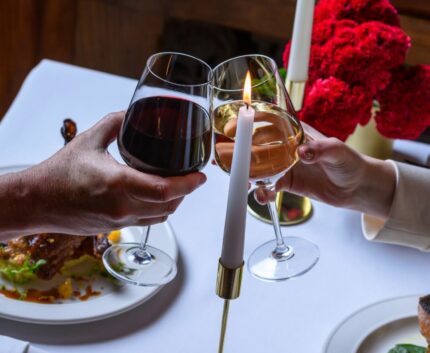 Cosy dining with candlelit wine, warm ambiance, elegant table setting, and vibrant red flowers at hotel restaurant.