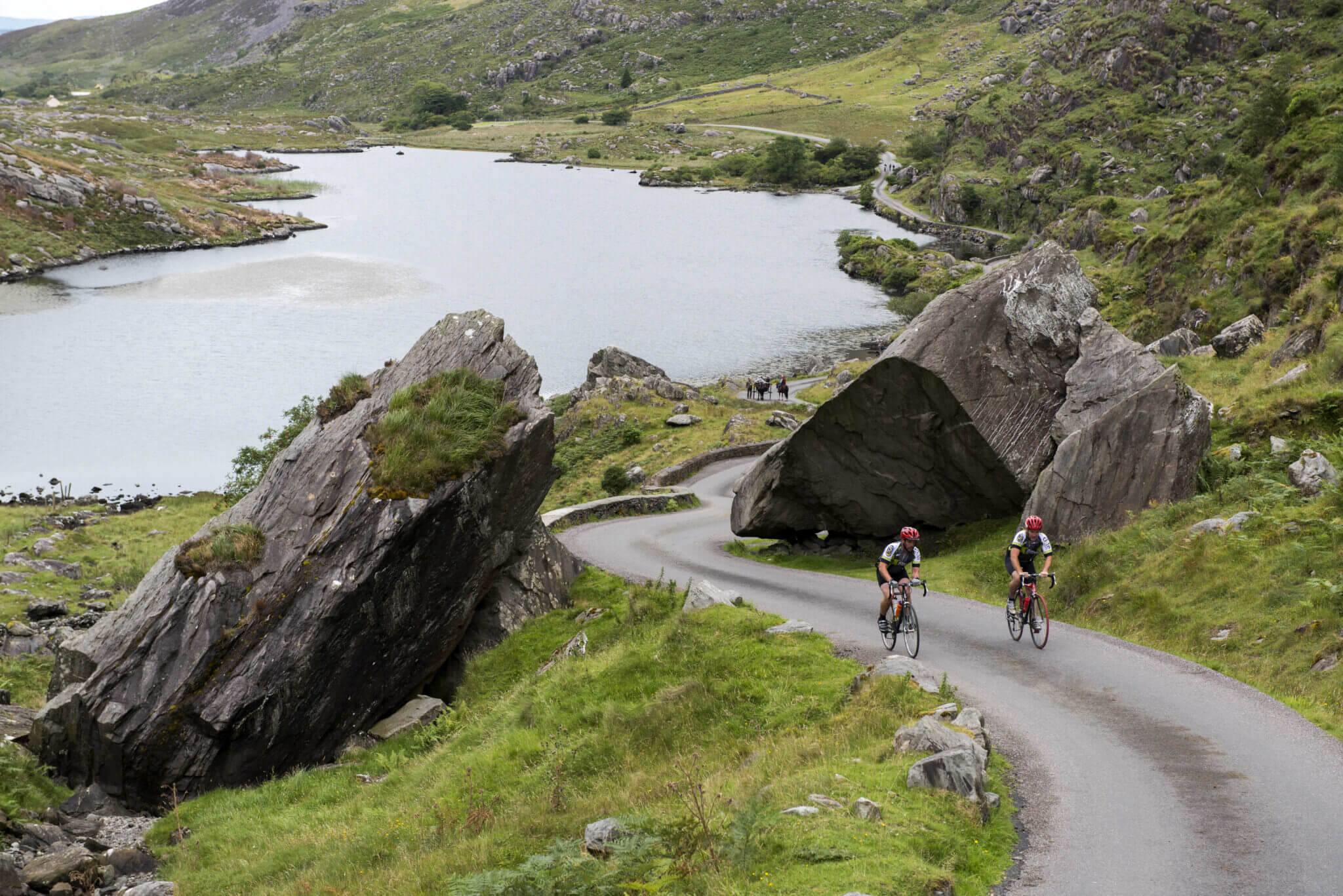 Cyclists enjoy scenic route by serene lake and lush hills near luxury countryside hotel with biking amenities.