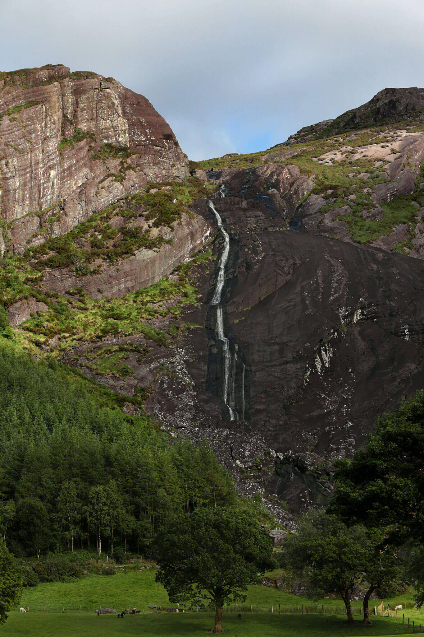 Idyllic waterfall cascading down lush green cliffs, surrounded by serene forest, offering a tranquil retreat for nature lovers.