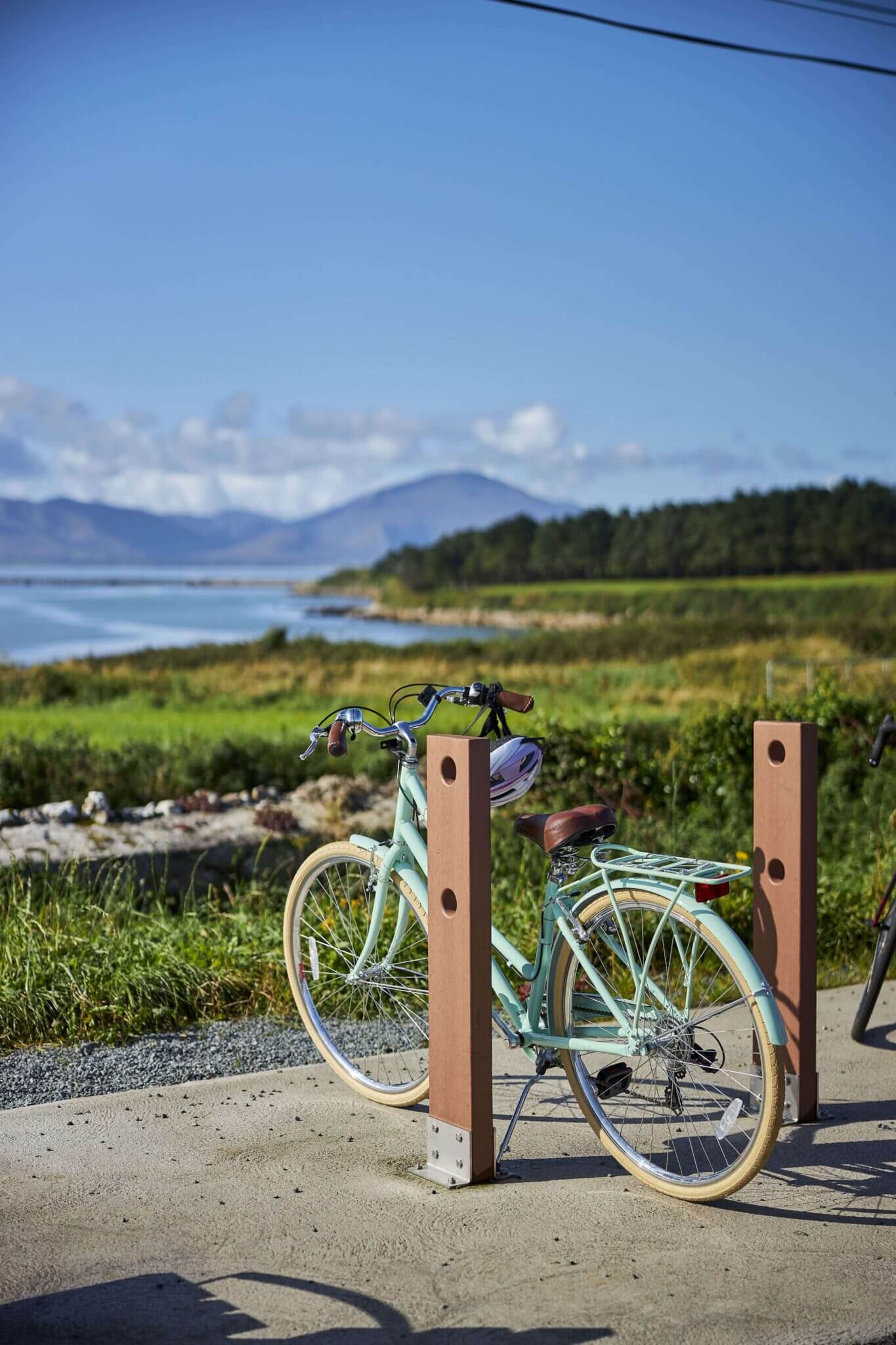 Scenic coastal view with mountains and a parked bicycle, ideal for biking enthusiasts; lush greenery and blue skies.