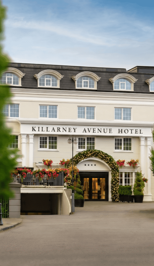 Elegant hotel entrance with floral decor, welcoming ambiance, and lush greenery under a clear blue sky.