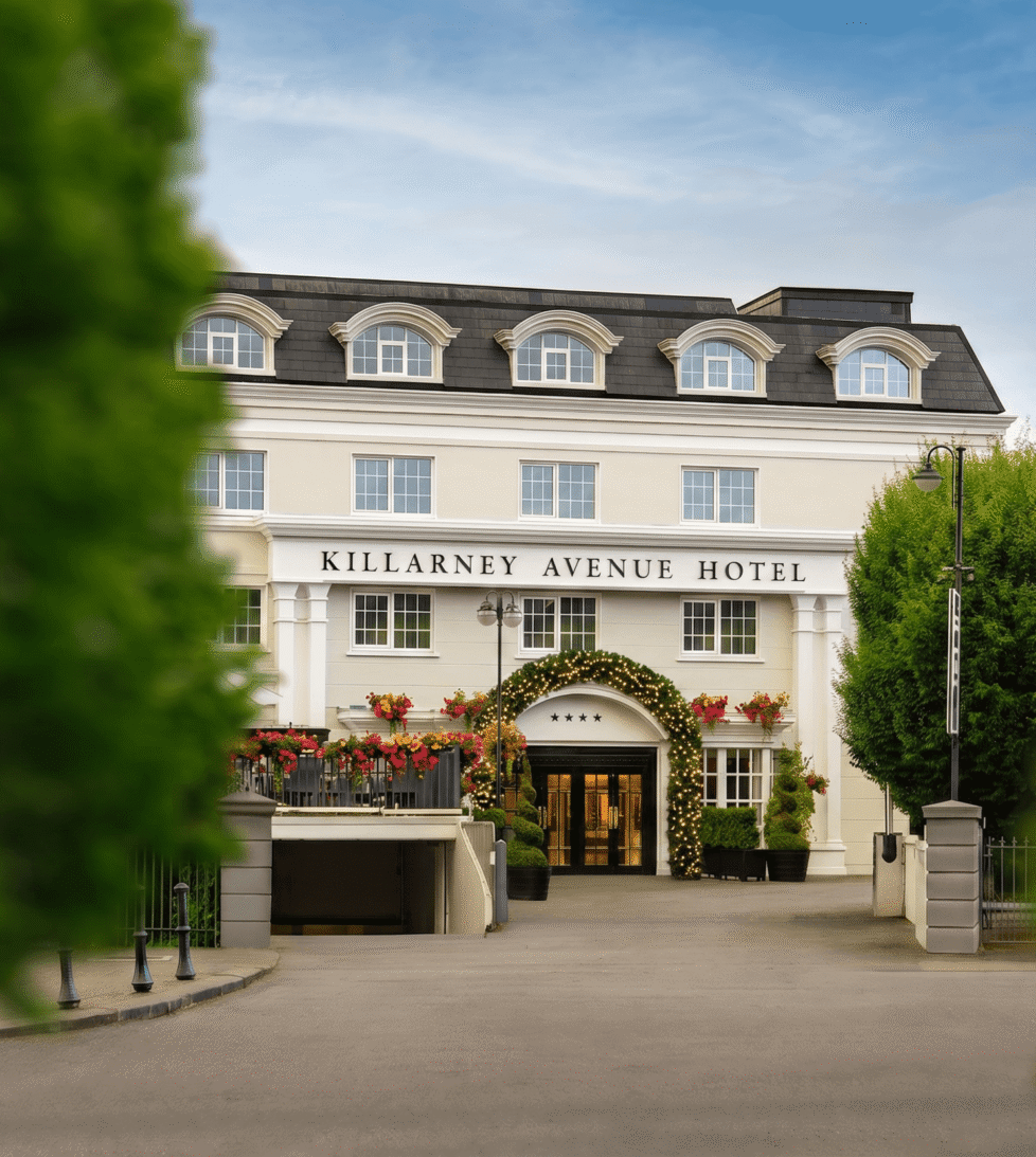 Elegant hotel entrance with floral decor, welcoming ambiance, and lush greenery under a clear blue sky.