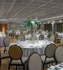 Elegant hotel ballroom set for banquet with round tables, floral centrepieces, and soft lighting.