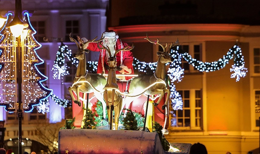 Festive street at night with illuminated Christmas lights, decorative reindeer and Santa display outside town centre hotel, cosy atmosphere